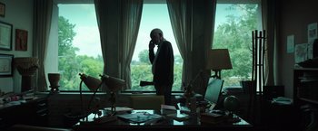 Movie still from “The Ritual Killer” (2023), directed by George Gallo – An older man standing in front of a window talking on a phone; Wide shot, Low angle