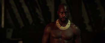 Movie still from “The Ritual Killer” (2023), directed by George Gallo – A man wearing a gold necklace is standing in a dimly lit room; Close Up shot, Low angle