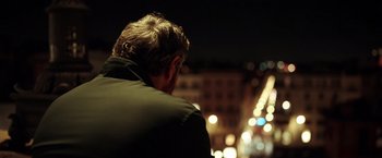 Movie still from “The Ritual Killer” (2023), directed by George Gallo – A man sitting on the side of the street at night; Medium shot, Over the shoulder angle