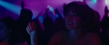Movie still from “The Royal Hotel” (2023), directed by Kitty Green – A woman smiles brightly at a concert with purple lights in the background; Close Up shot, Over the shoulder angle