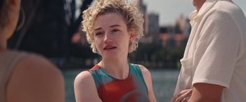 Movie still from “The Royal Hotel” (2023), directed by Kitty Green – A woman with blonde curly hair wearing a red and blue top; Close Up shot, Over the shoulder angle
