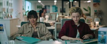 Movie still from “The Royal Hotel” (2023), directed by Kitty Green – Two women sitting at a desk in an office setting; Medium shot, High angle