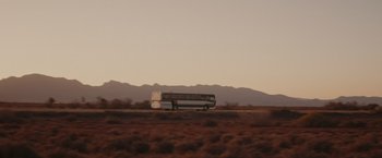 Movie still from “The Royal Hotel” (2023), directed by Kitty Green – A bus driving down a road in the middle of the desert; Extreme Wide shot, Low angle
