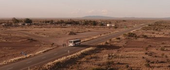 Movie still from “The Royal Hotel” (2023), directed by Kitty Green – A bus driving down a road in the middle of the desert; Extreme Wide shot, High angle