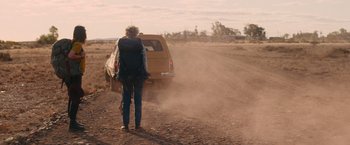 Movie still from “The Royal Hotel” (2023), directed by Kitty Green – A man with a backpack is standing in front of a car; Wide shot, Over the shoulder angle