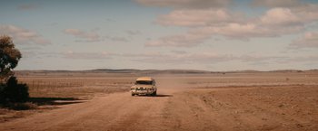 Movie still from “The Royal Hotel” (2023), directed by Kitty Green – A truck driving down a dirt road in the middle of the desert; Extreme Wide shot, Low angle