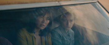 Movie still from “The Royal Hotel” (2023), directed by Kitty Green – Two young people sitting next to each other on a bus; Close Up shot, Over the shoulder angle