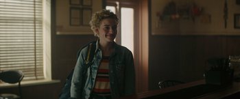 Movie still from “The Royal Hotel” (2023), directed by Kitty Green – A woman standing next to a window in a room; Medium shot, Over the shoulder angle