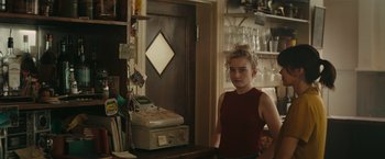Movie still from “The Royal Hotel” (2023), directed by Kitty Green – A woman standing in front of a cash register in a kitchen; Medium shot, Over the shoulder angle