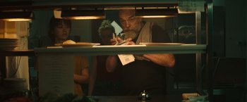 Movie still from “The Royal Hotel” (2023), directed by Kitty Green – A man writing on a piece of paper in front of a woman; Close Up shot, Over the shoulder angle