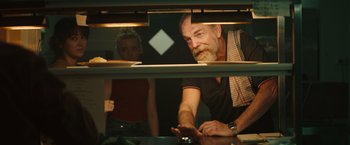 Movie still from “The Royal Hotel” (2023), directed by Kitty Green – A man and a woman are looking at something in a display case; Close Up shot, Over the shoulder angle
