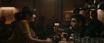 Movie still from “The Royal Hotel” (2023), directed by Kitty Green – A group of people sitting at a table drinking beer; Medium shot, Over the shoulder angle