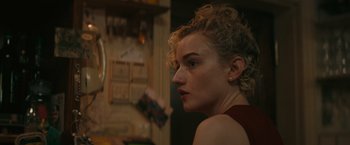 Movie still from “The Royal Hotel” (2023), directed by Kitty Green – A person with curly blonde hair; Close Up shot, Over the shoulder angle