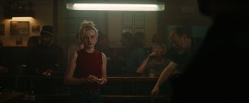 Movie still from “The Royal Hotel” (2023), directed by Kitty Green – A woman standing in front of a group of people in a room; Medium shot, Over the shoulder angle