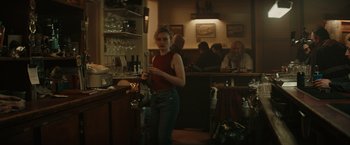 Movie still from “The Royal Hotel” (2023), directed by Kitty Green – A woman standing at a bar holding a wine glass; Medium shot, Over the shoulder angle