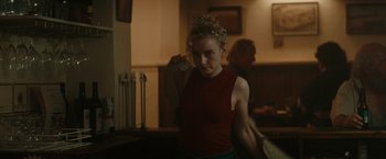 Movie still from “The Royal Hotel” (2023), directed by Kitty Green – A woman in a red shirt is standing in front of a mirror; Medium shot, Over the shoulder angle