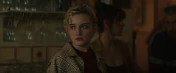 Movie still from “The Royal Hotel” (2023), directed by Kitty Green – A woman in a red shirt is looking at the camera; Close Up shot, Over the shoulder angle