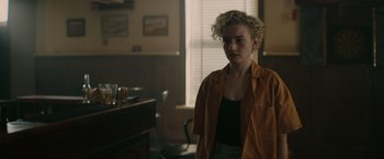 Movie still from “The Royal Hotel” (2023), directed by Kitty Green – A woman standing in front of a window in a room; Medium shot, Over the shoulder angle