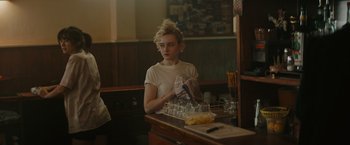 Movie still from “The Royal Hotel” (2023), directed by Kitty Green – A woman sitting at a counter with a bunch of empty glasses; Medium shot, Over the shoulder angle