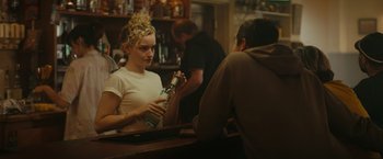 Movie still from “The Royal Hotel” (2023), directed by Kitty Green – A woman is holding a bottle of beer in her hand; Medium shot, Over the shoulder angle