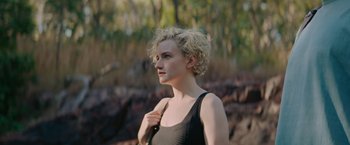 Movie still from “The Royal Hotel” (2023), directed by Kitty Green – A woman with blonde curly hair wearing a black top; Medium shot, Low angle