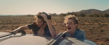 Movie still from “The Royal Hotel” (2023), directed by Kitty Green – Two women in the back seat of a car laughing; Medium shot, High angle