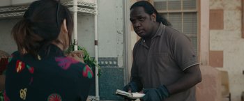 Movie still from “The Royal Hotel” (2023), directed by Kitty Green – A man is reading a book while standing next to a potted plant; Medium shot, Over the shoulder angle