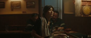 Movie still from “The Royal Hotel” (2023), directed by Kitty Green – A woman standing in front of two men at a bar; Medium shot, Over the shoulder angle