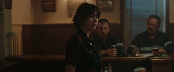 Movie still from “The Royal Hotel” (2023), directed by Kitty Green – A woman standing in front of a man in a bar; Medium shot, Over the shoulder angle