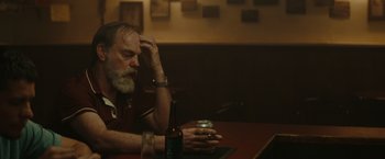 Movie still from “The Royal Hotel” (2023), directed by Kitty Green – An older man sitting at a table with a beer in front of him; Close Up shot, Over the shoulder angle