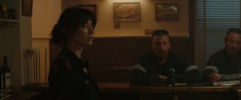 Movie still from “The Royal Hotel” (2023), directed by Kitty Green – A man and a woman sitting at a wooden table; Medium shot, Over the shoulder angle