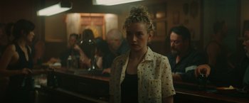 Movie still from “The Royal Hotel” (2023), directed by Kitty Green – A woman standing in front of a group of people; Medium shot, Over the shoulder angle