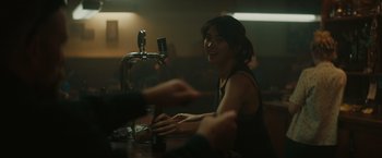 Movie still from “The Royal Hotel” (2023), directed by Kitty Green – A woman sitting at a table in front of a beer dispenser; Close Up shot, Over the shoulder angle