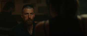 Movie still from “The Royal Hotel” (2023), directed by Kitty Green – A man with a shaved head is looking at a woman; Close Up shot, Over the shoulder angle