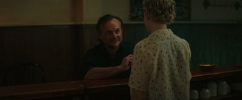 Movie still from “The Royal Hotel” (2023), directed by Kitty Green – A man sitting in front of a woman in front of a mirror; Medium shot, Over the shoulder angle