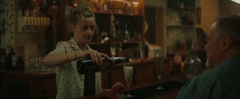 Movie still from “The Royal Hotel” (2023), directed by Kitty Green – A woman pouring a glass of wine at a bar; Medium shot, Over the shoulder angle
