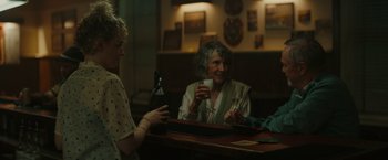 Movie still from “The Royal Hotel” (2023), directed by Kitty Green – A group of people sitting at a table with drinks; Medium shot, Over the shoulder angle