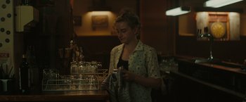 Movie still from “The Royal Hotel” (2023), directed by Kitty Green – A woman is looking at a napkin in a store; Medium shot, Over the shoulder angle