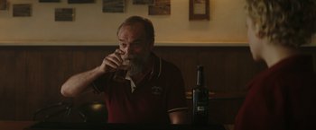 Movie still from “The Royal Hotel” (2023), directed by Kitty Green – An older man sitting in front of a bottle of wine; Close Up shot, Over the shoulder angle