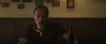 Movie still from “The Royal Hotel” (2023), directed by Kitty Green – An older man sitting in front of a bottle of wine; Medium shot, Low angle