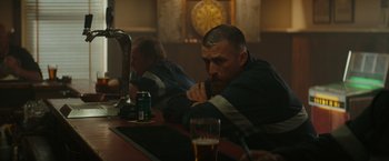 Movie still from “The Royal Hotel” (2023), directed by Kitty Green – A man sitting at a table with a beer in front of him; Medium shot, Over the shoulder angle