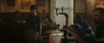 Movie still from “The Royal Hotel” (2023), directed by Kitty Green – A group of people sitting at a table in a room; Medium shot, Over the shoulder angle