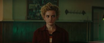 Movie still from “The Royal Hotel” (2023), directed by Kitty Green – A woman with blonde curly hair is looking at the camera; Close Up shot, Over the shoulder angle