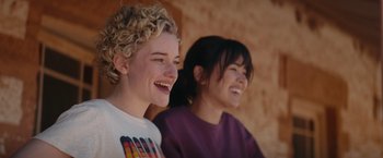 Movie still from “The Royal Hotel” (2023), directed by Kitty Green – Two young women laughing together while sitting next to each other; Close Up shot, Over the shoulder angle