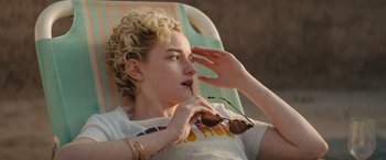 Movie still from “The Royal Hotel” (2023), directed by Kitty Green – A woman sitting in a chair holding a pair of sunglasses; Close Up shot, Over the shoulder angle