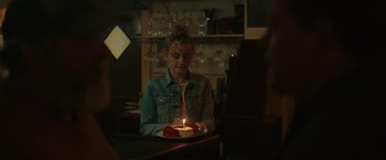 Movie still from “The Royal Hotel” (2023), directed by Kitty Green – A woman sitting in front of a cake with a lit candle on it; Close Up shot, Over the shoulder angle