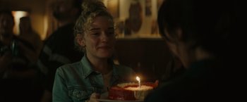 Movie still from “The Royal Hotel” (2023), directed by Kitty Green – A woman is holding a cake with a lit candle; Close Up shot, Over the shoulder angle