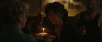 Movie still from “The Royal Hotel” (2023), directed by Kitty Green – A woman smiles as she blows out a candle on a birthday cake; Close Up shot, Over the shoulder angle