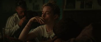 Movie still from “The Royal Hotel” (2023), directed by Kitty Green – A woman eating a piece of food while sitting at a table; Close Up shot, Over the shoulder angle
