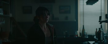 Movie still from “The Royal Hotel” (2023), directed by Kitty Green – A woman standing in a dark room looking at the camera; Close Up shot, Over the shoulder angle